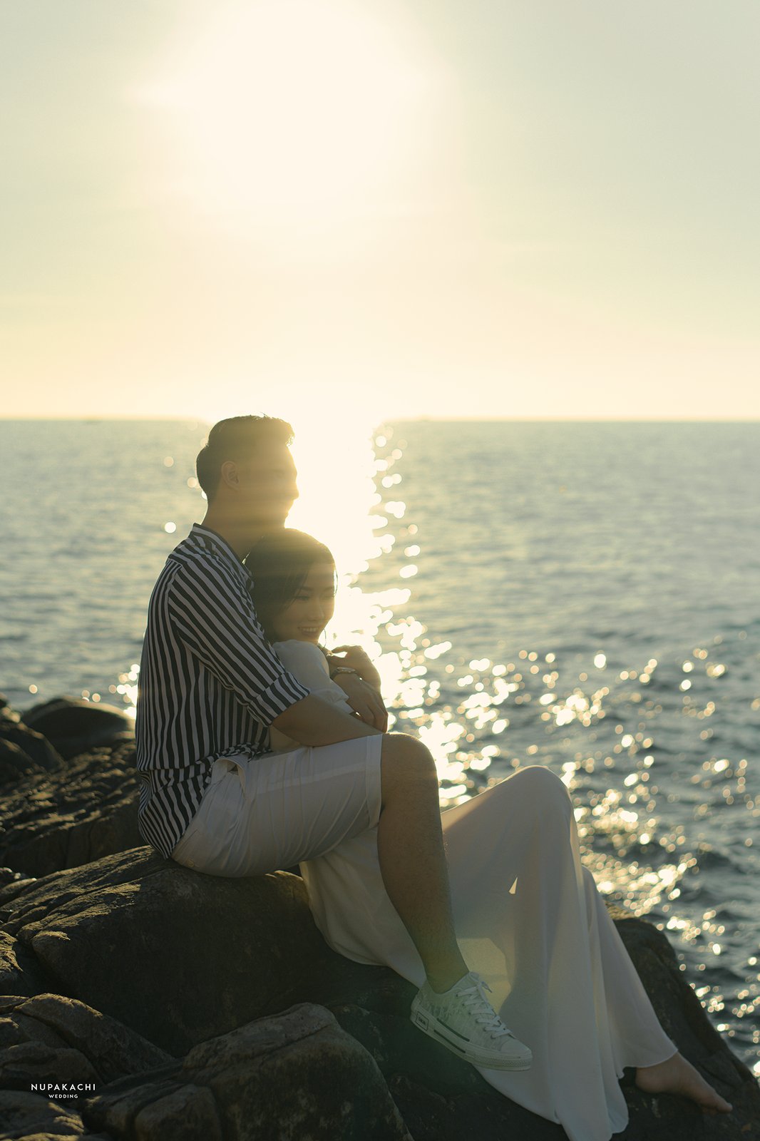 Couple sitting on seaside rocks at golden hour, destination pre-wedding photography Vietnam