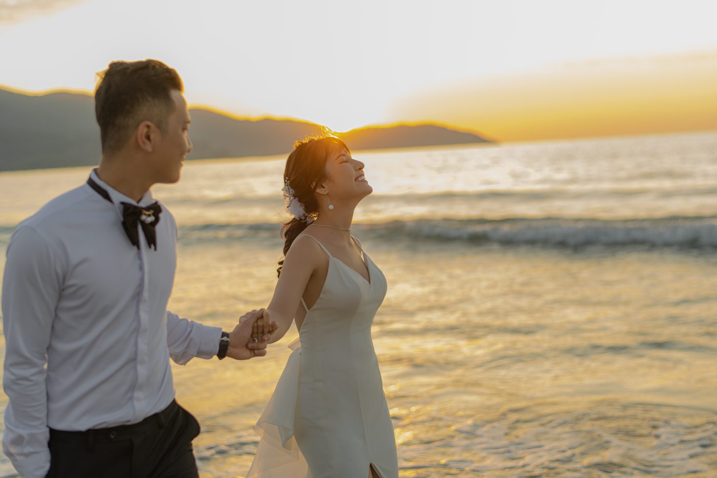 Cặp đôi nắm tay chạy trên bãi cát ướt lúc mặt trời lặn, Đà Nẵng