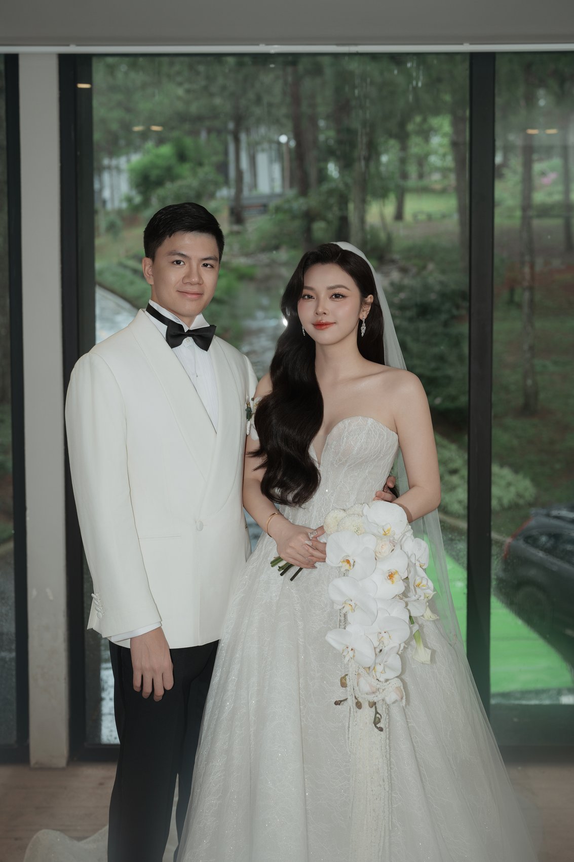 Bride and groom in white by the glasshouse at a pine forest destination wedding, Vietnam