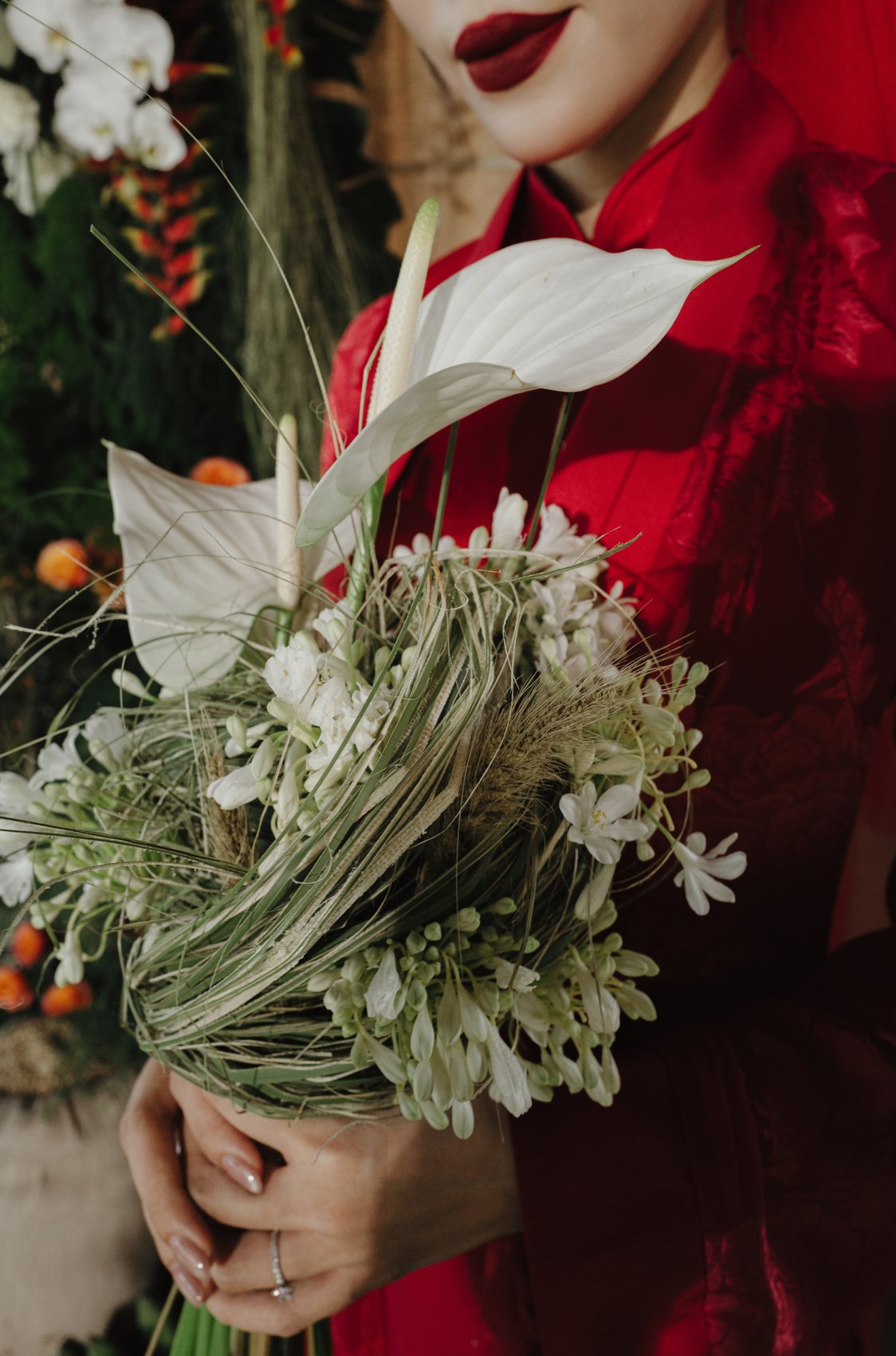 Bridal bouquet in hands, red ao dai detail at a Vietnamese destination wedding