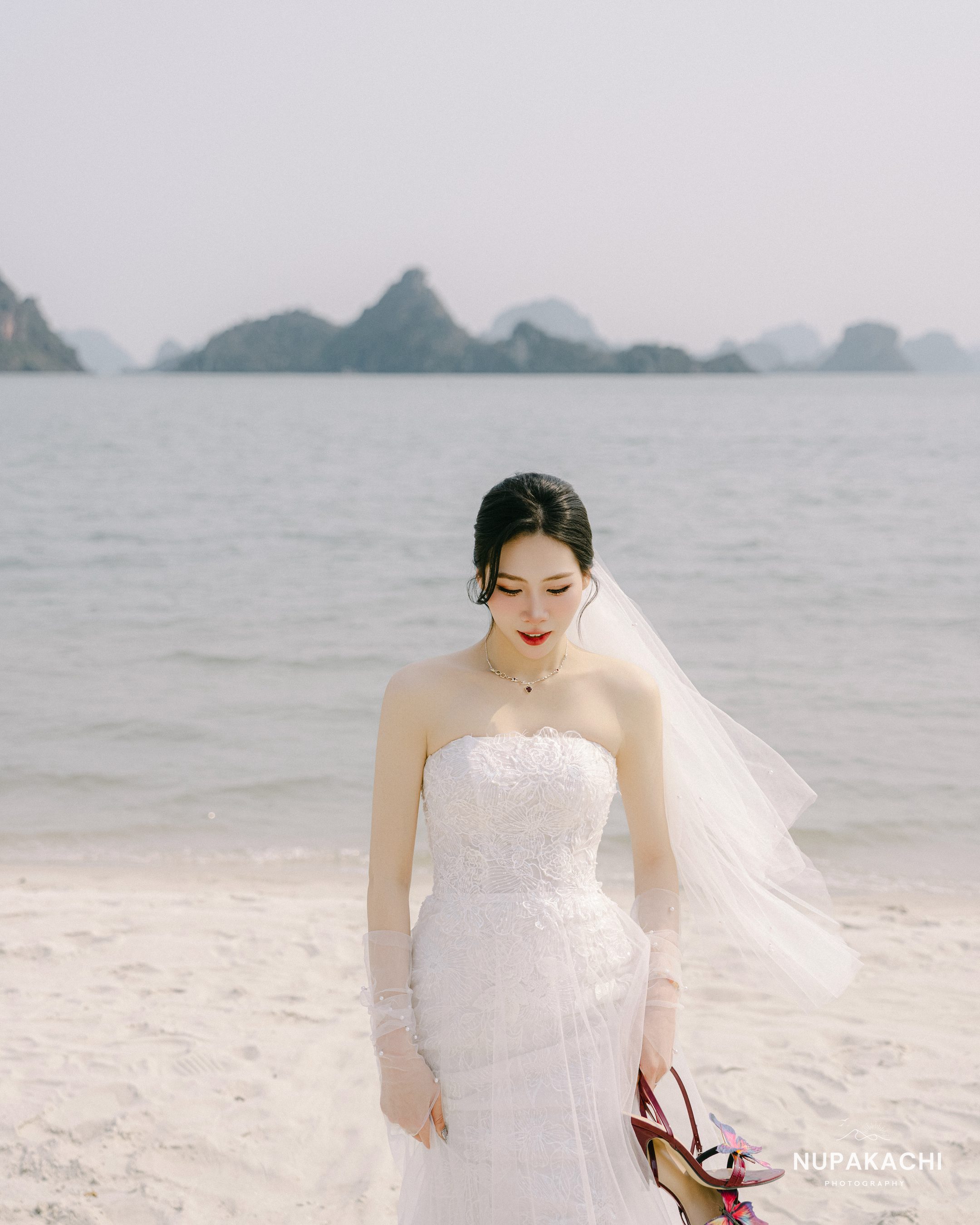 Cô dâu cầm giày cưới đứng trên cát trắng Hạ Long
