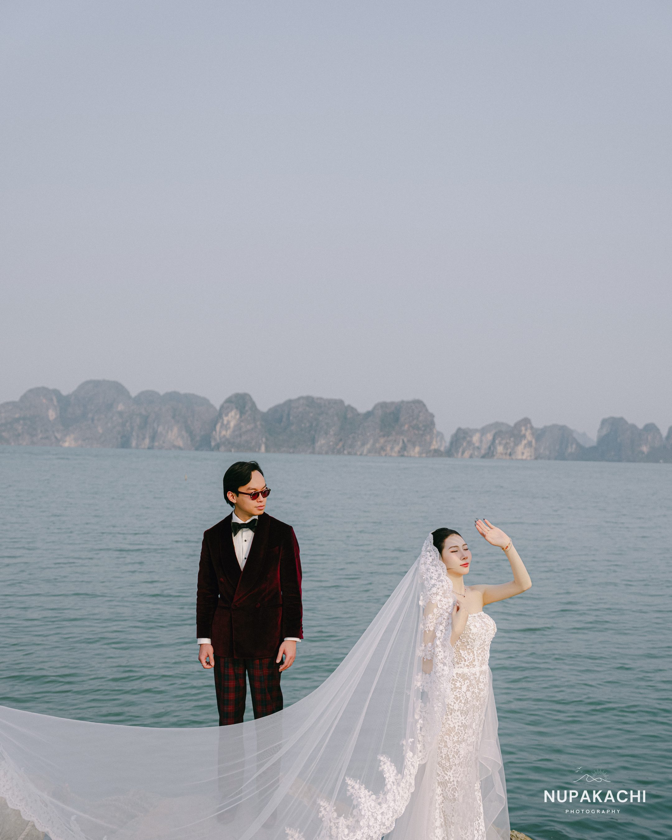 Chú rể vest nhung đỏ đứng giữa vịnh với núi đá vôi phía sau