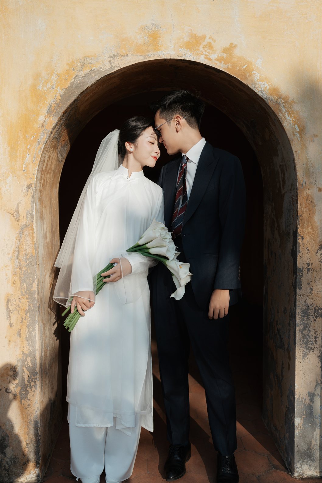 Cô dâu áo dài trắng và chú rể dưới cổng vòm cổ Hoàng Thành Thăng Long, chụp ảnh cưới Hà Nội