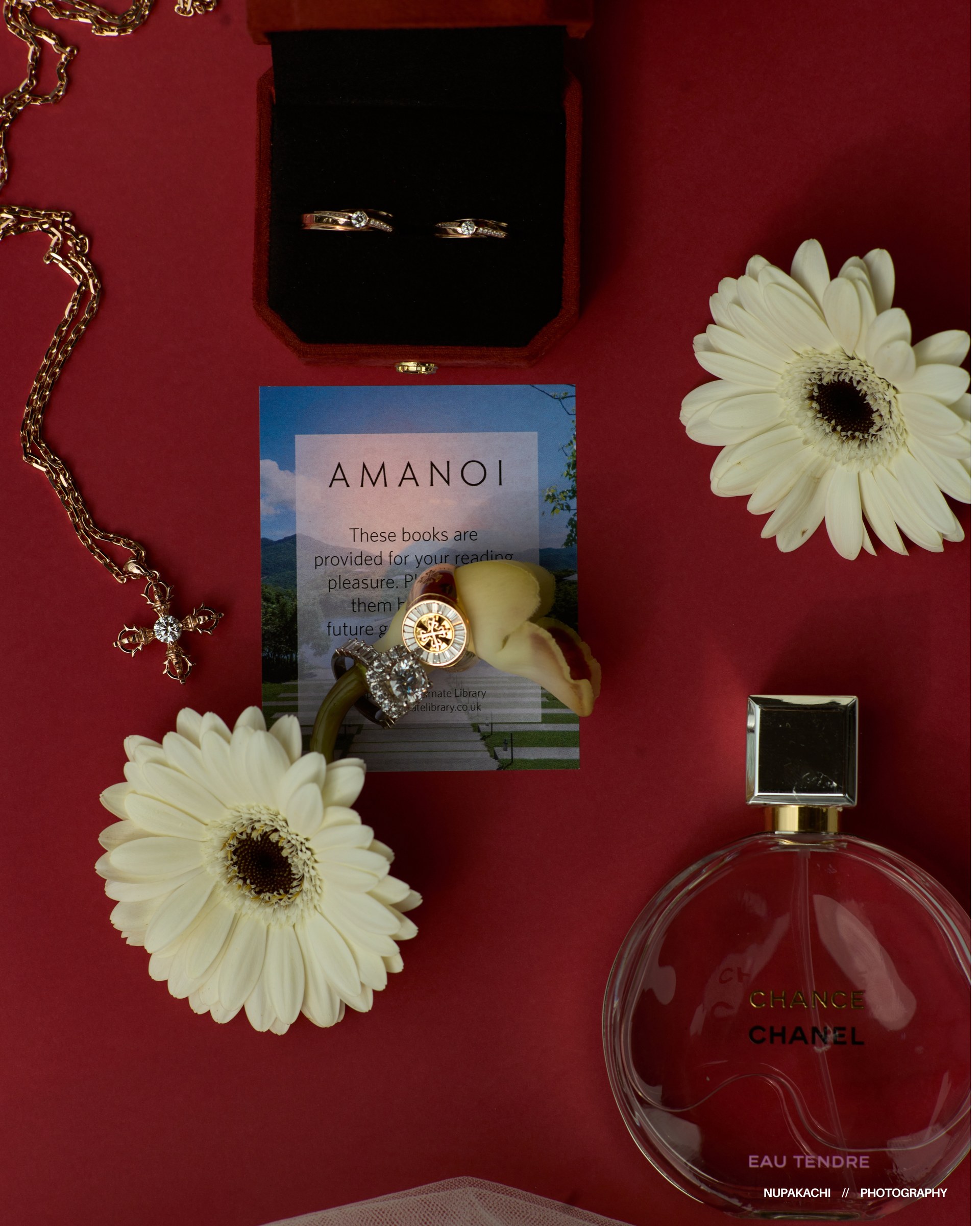 Wedding rings, perfume and white gerbera flat lay on red, bridal accessories styled by Nupakachi at Amanoi Vietnam