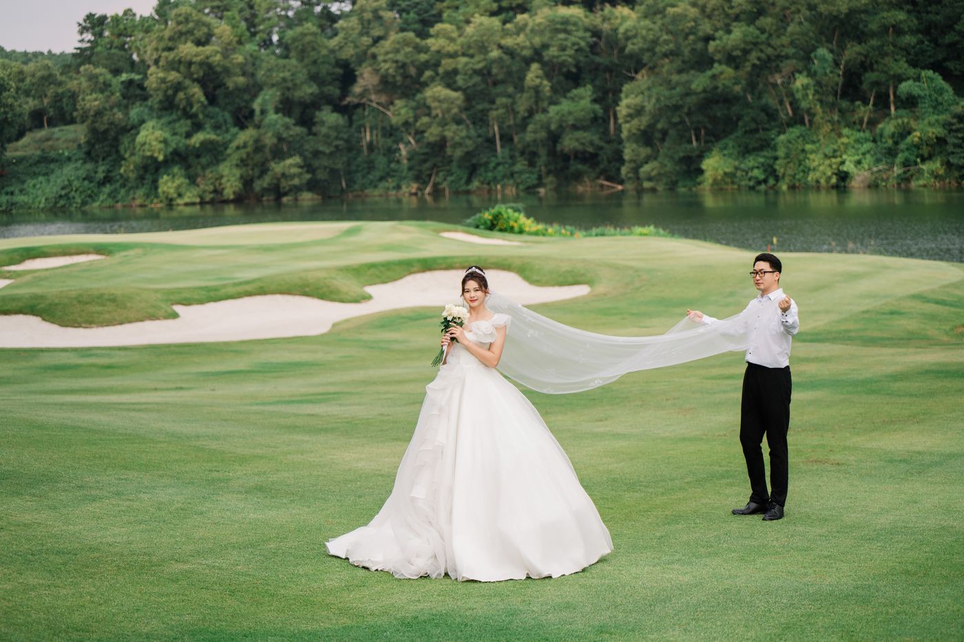 Chú rể cầm voan dài của cô dâu trên thảm cỏ sân golf Tràng An