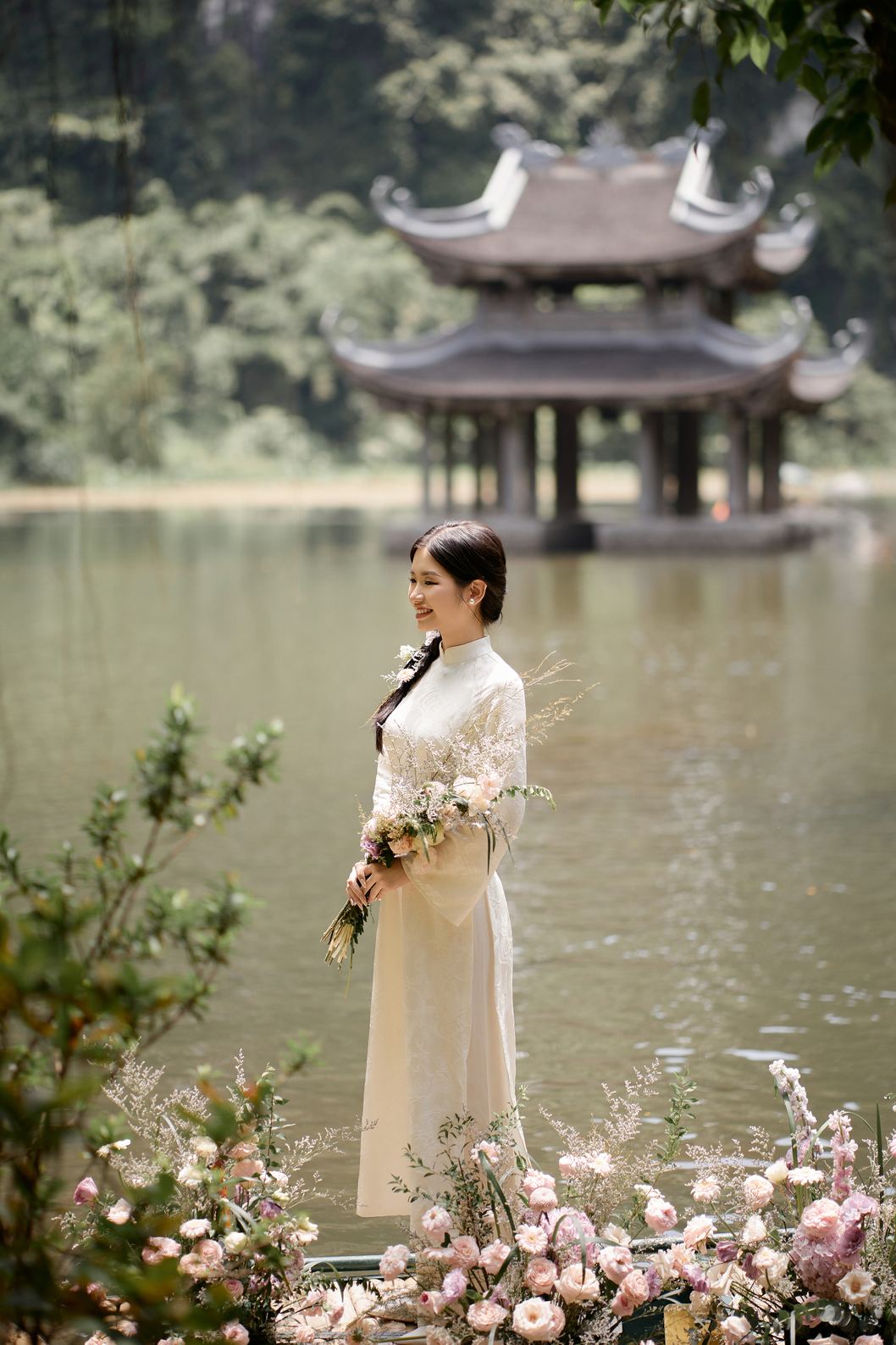Cô dâu áo dài trắng đứng bên hồ trước thủy đình Tràng An