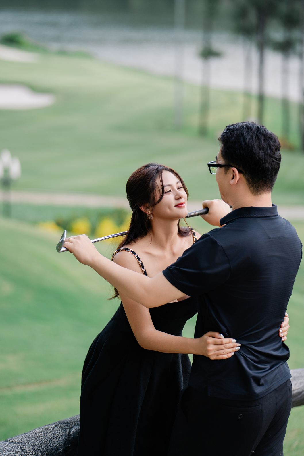 Cặp đôi mặc đồ thường màu đen, tay cầm gậy golf trên sân golf Tràng An