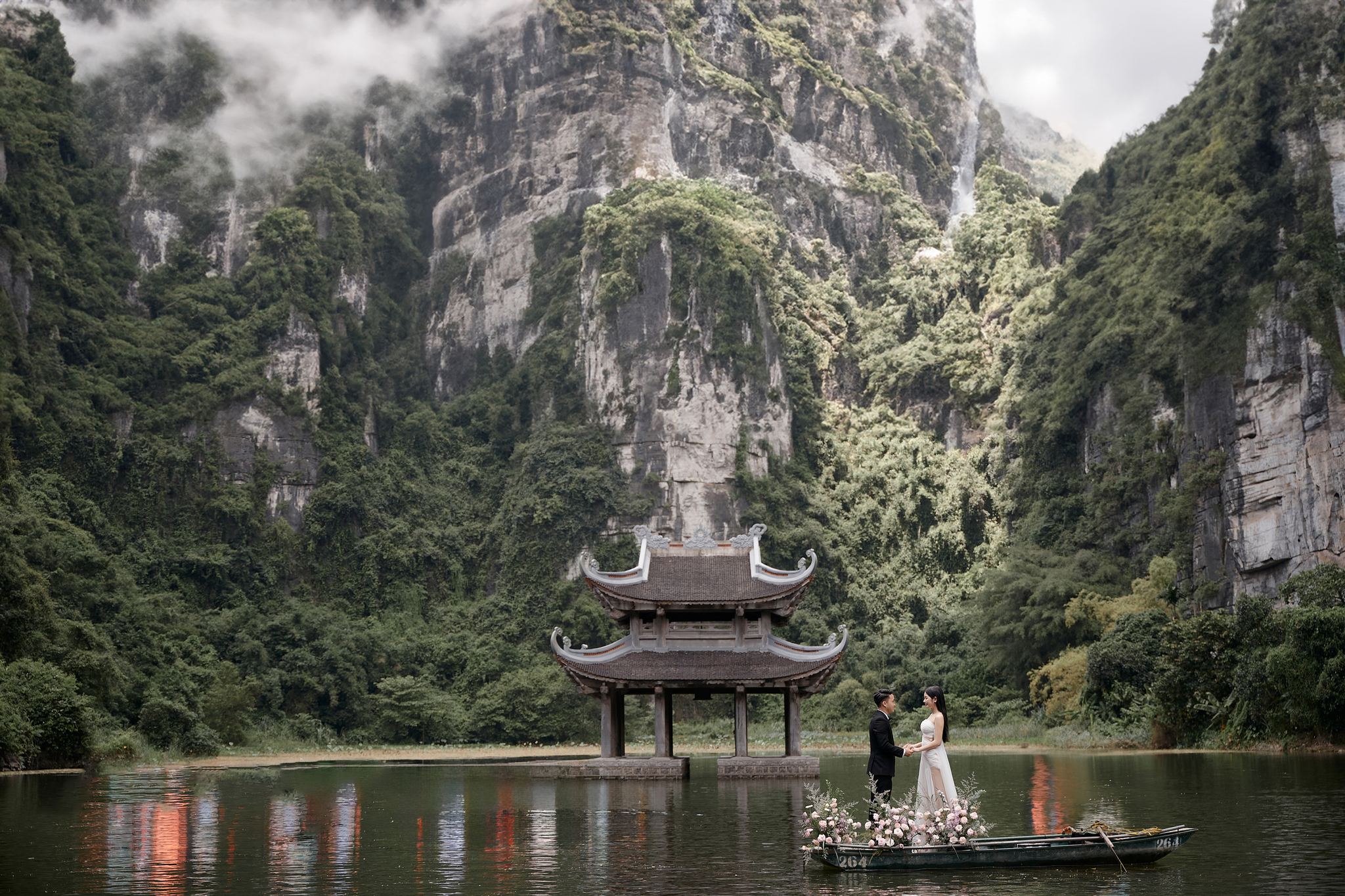 Cặp đôi trên thuyền kết hoa trước thủy đình và vách núi đá Tràng An, chụp ảnh cưới Ninh Bình