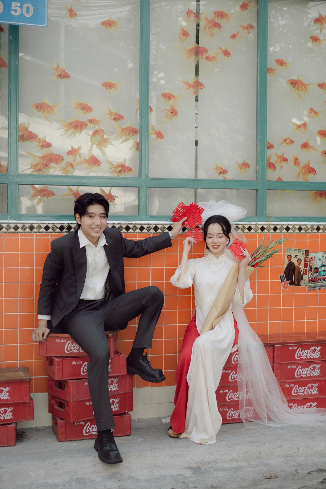 Cặp đôi ngồi trên két nước ngọt đỏ bên tường gạch cam, prewedding Sài Gòn