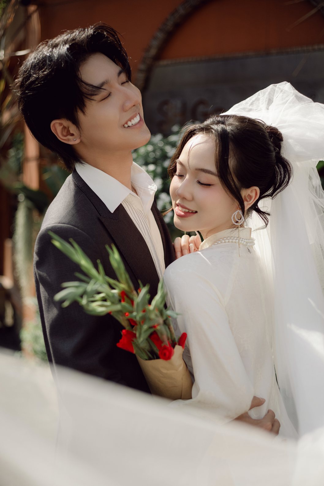 Cô dâu áo dài cầm bó hoa đỏ bên chú rể, chụp ảnh cưới Sài Gòn