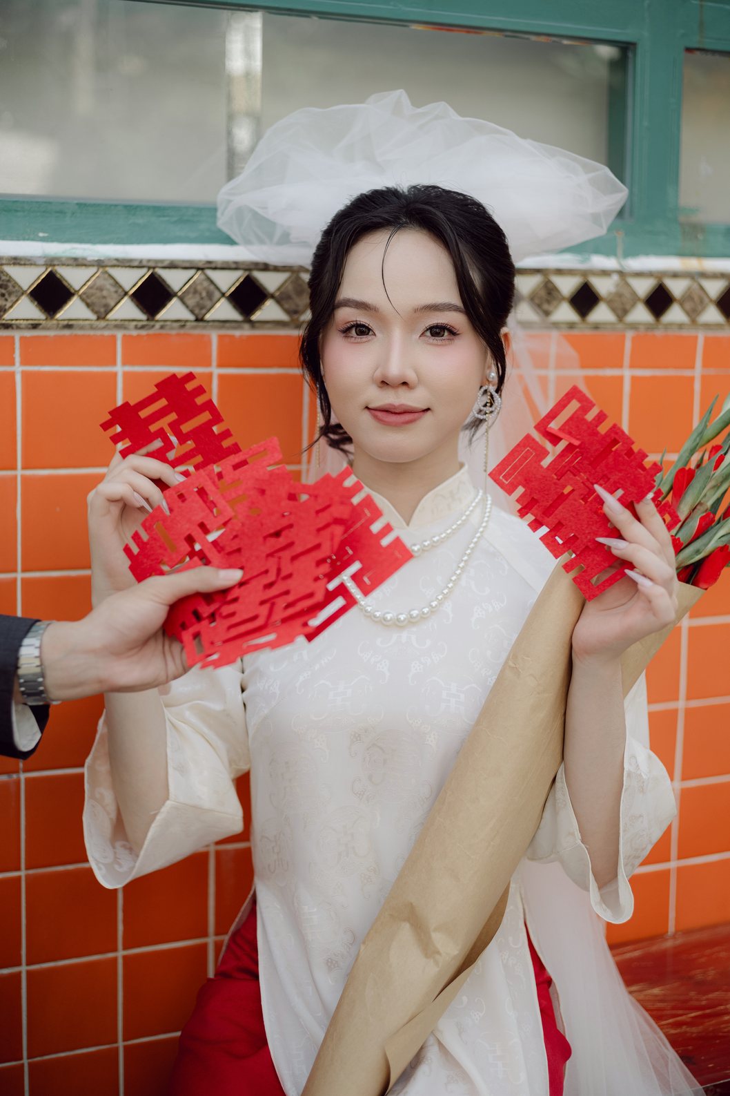 Cô dâu áo dài trắng cầm bao lì xì đỏ bên tường gạch cam Quận 2, prewedding Sài Gòn
