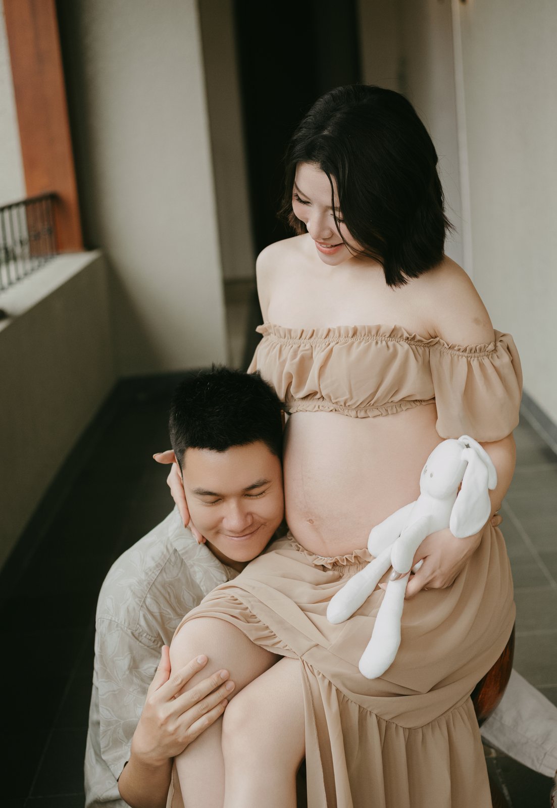 Expecting mother held by her husband with a bunny toy, maternity photography Vietnam