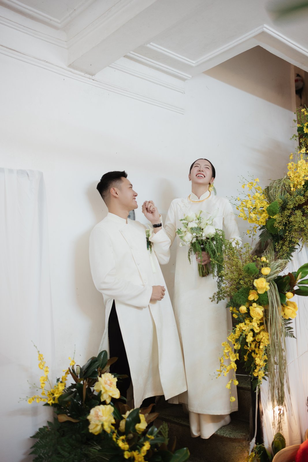 Couple in white ao dai under yellow flowers at the family home ceremony, Vietnam
