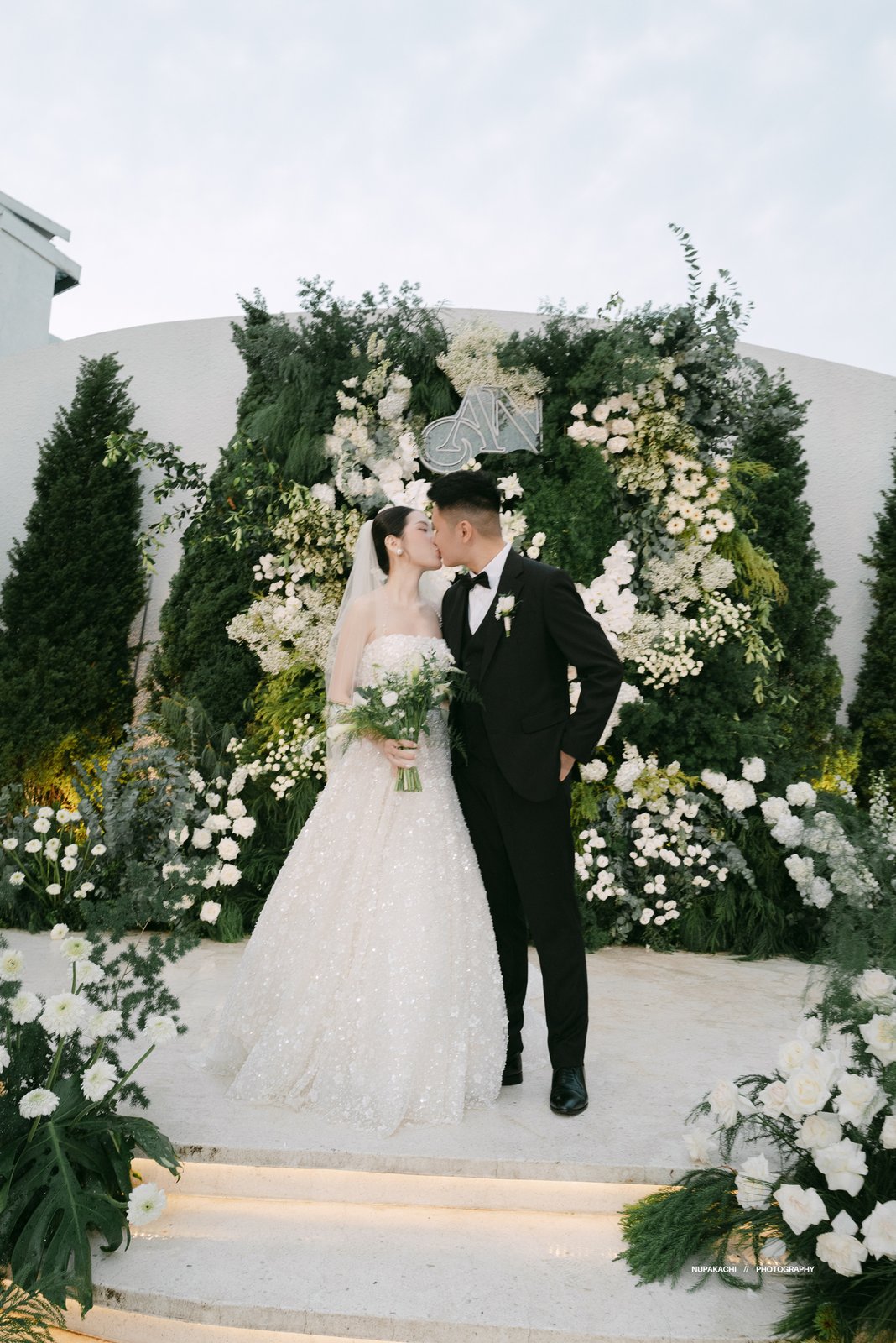 First kiss at a white garden ceremony among evergreen trees, Vietnam wedding