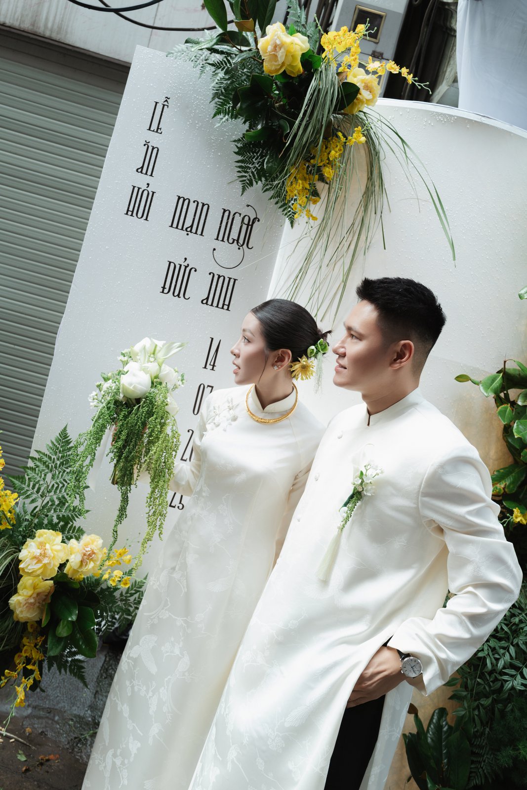 Bride and groom in white ao dai at the flower gate of their family home ceremony, Vietnam
