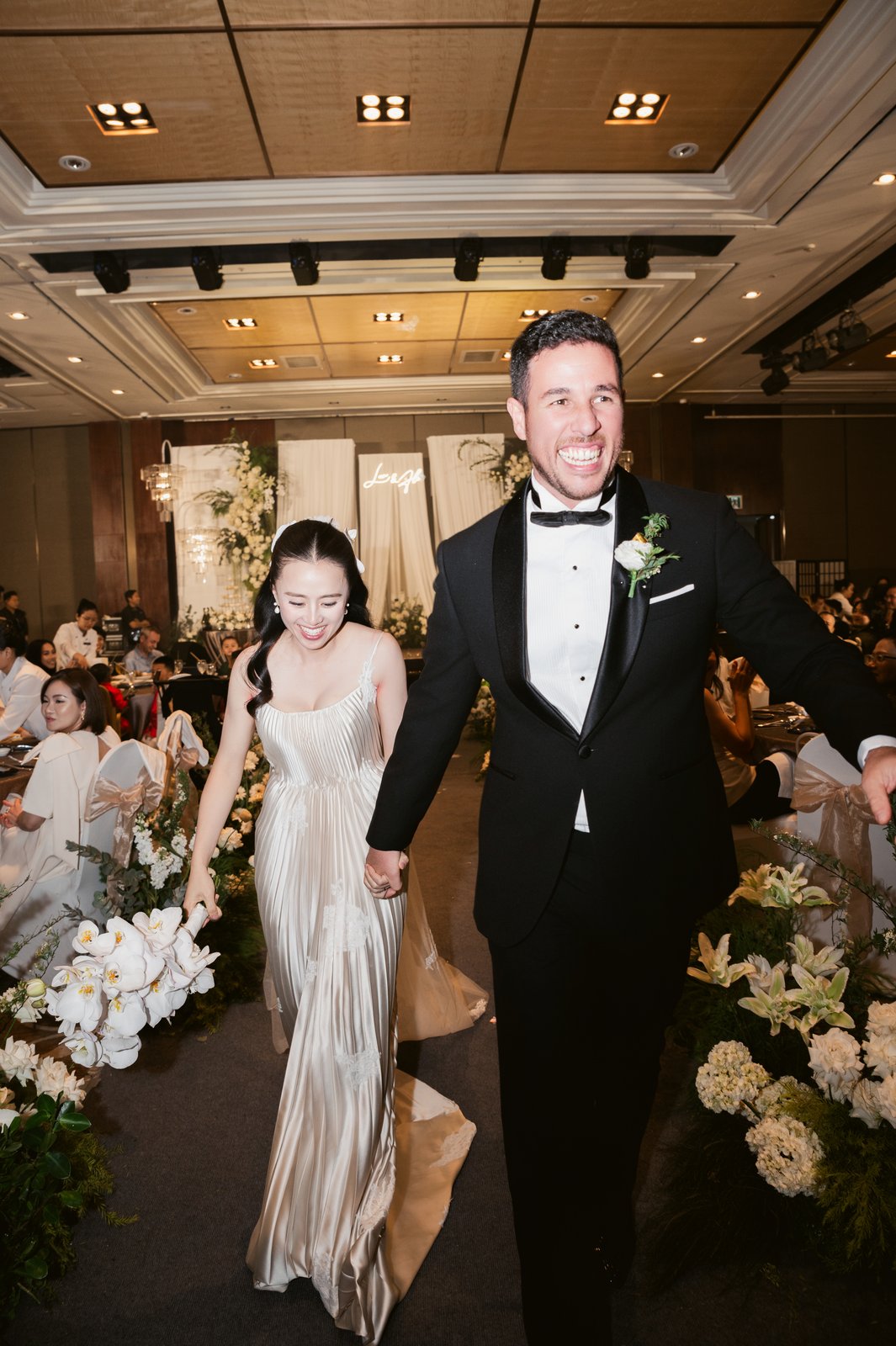 Bride and groom walking the aisle with joyful guests, wedding reception Vietnam