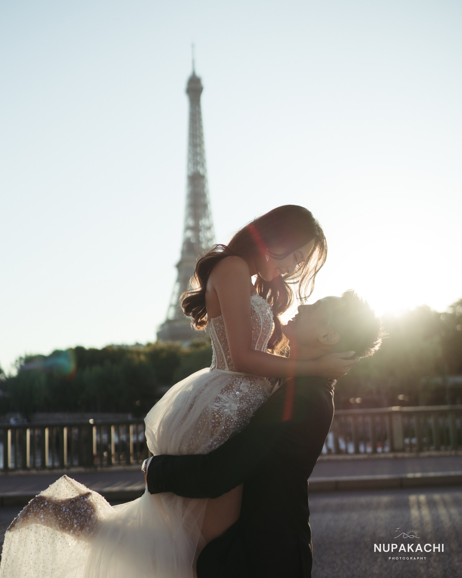 Groom lifting bride under the Eiffel Tower, joyful Paris pre-wedding