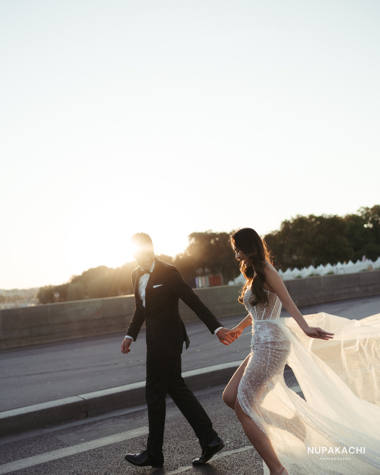 Couple walking at sunset on a Paris bridge, wedding dress flowing